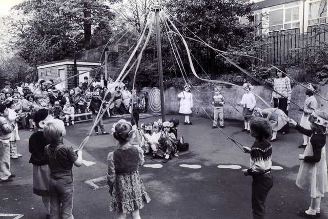 Children of Hucklow First School, Firth Park, dance around the maypole before an audience of parents in the school yard in May 1983