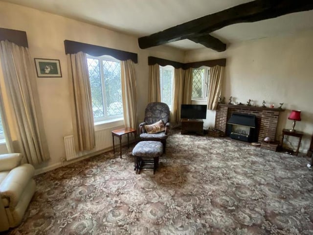 An entrance hall, which boasts a storage cupboard and access to the loft via a pull-down ladder, leads to this large lounge or living room. It has a feature fireplace, four uPVC windows and a radiator.