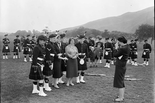 The 7/9th Battalion Royal Scots pose for a picture with a tourist during their rehearse for their Golden Jubilee Parade in Holyrood Park in June 1958.