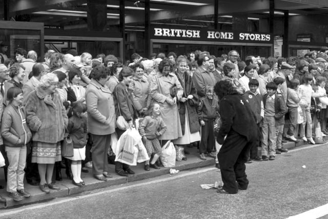 Crowds outside British Home Stores in Princes Street  watch the Edinburgh University Charities Week parade, May 1983. A little girl mimics the actions of a student in a gorilla suit.