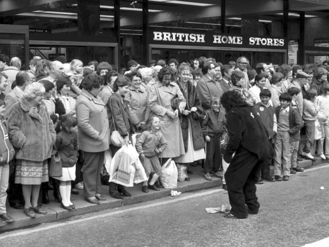Crowds outside British Home Stores in Princes Street watch the Edinburgh University Charities Week parade, May 1983. A little girl mimics the actions of a student in a gorilla suit.