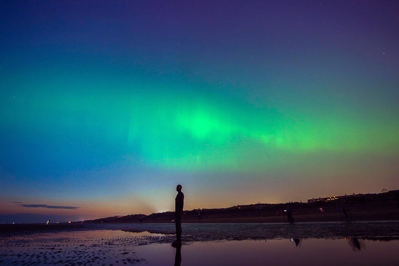 The aurora borealis, also known as the northern lights, glow on the horizon at Another Place by Anthony Gormley, Crosby Beach, Liverpool , Merseyside .