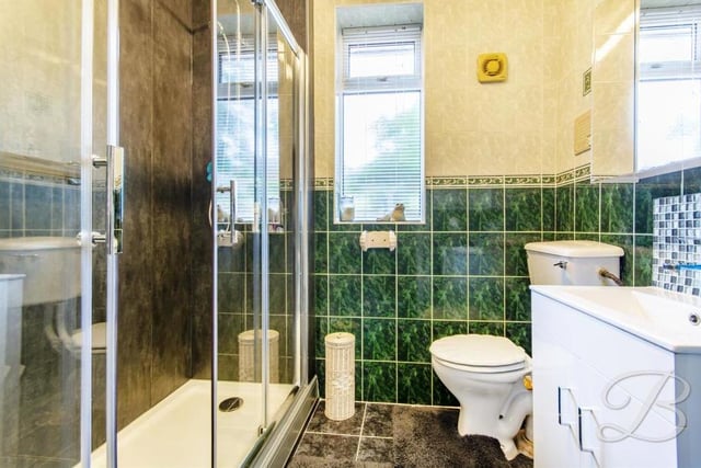 Here is the shower room, which can be accessed via a hallway that leads to all three bedrooms. It is a fully-tiled suite comprising enclosed shower, low-flush WC, vanity unit with wash hand basin, and cupboard for storage.