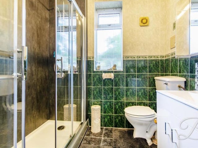 Here is the shower room, which can be accessed via a hallway that leads to all three bedrooms. It is a fully-tiled suite comprising enclosed shower, low-flush WC, vanity unit with wash hand basin, and cupboard for storage.