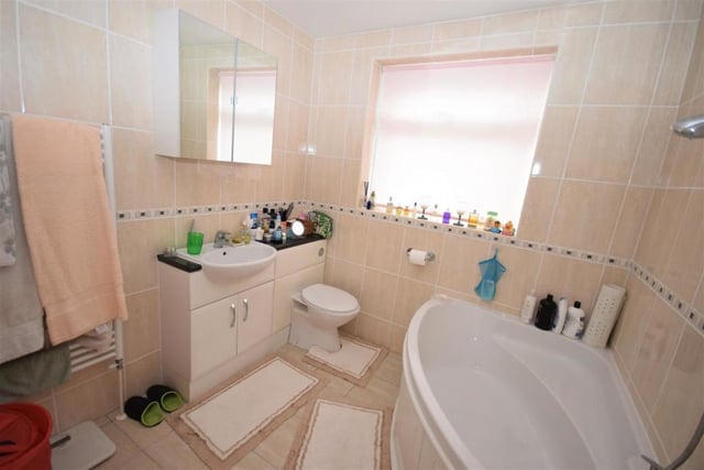 This is the en suite bathroom to the main bedroom. It is fitted with a panelled bath that has a shower above, a low-flush WC and wash basin in a vanity unit that also offers storage. The room is finished with tiled walls and floor.
