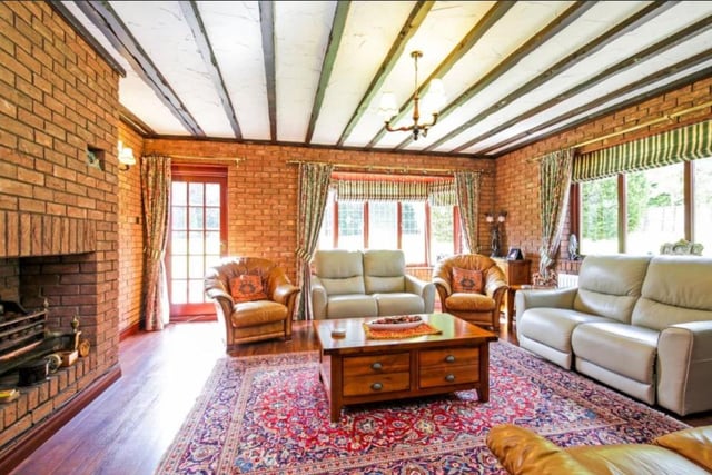 The living room features a rustic wooden beam ceiling and grand fireplace as well as lots of natural lighting.