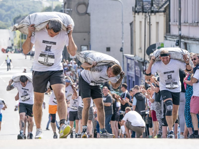 Competitors take part in the Scottish Coal Carrying Championships through the streets of Kelty in Fife. Picture date: Saturday August 28, 2021. PA Photo. The annual event is one of only two Coal Races in the world and the men's race requires participants to carry a 50-kilo bag of coal and the women's race requires a 25-kilo bag of coal to be carried over 1000 metres through the village. Photo credit should read: Jane Barlow/PA Wire