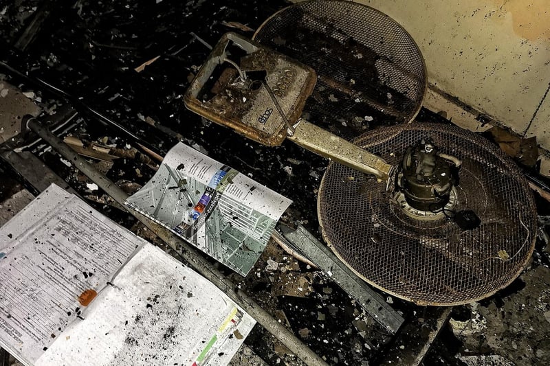 A broken fan and old paperwork litter the floor of the abandoned site.