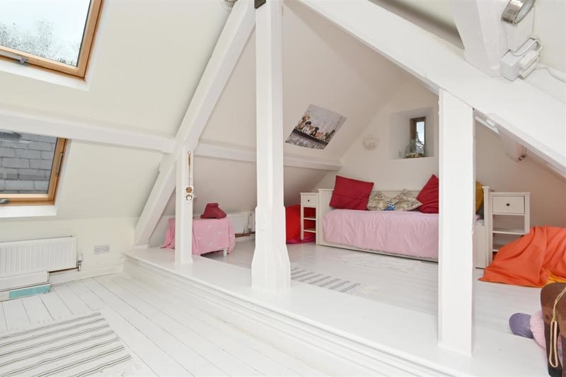 This bedroom has a white painted timber floor and solid timber trusses. Light floods into the room through the eight Velux windows and an original vertical stone mullion window.