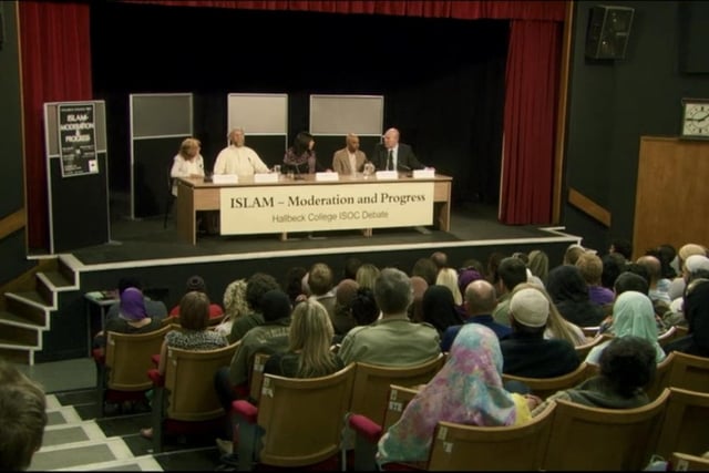 In the theatre scene Barry is talking on a panel on the moderation and progress of Islam in a conference in a university lecture theatre. This is where we first see actor Arsher Ali as Hassan Malik, a rapper who joins the cell after Barry witnesses him pretending to blow himself up at this conference.