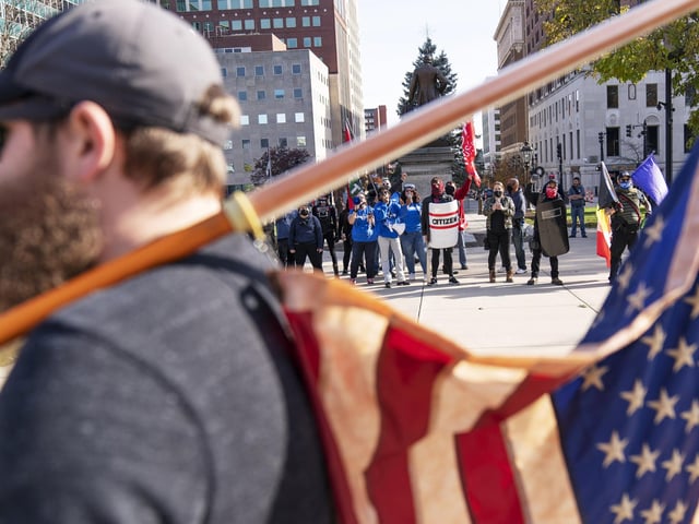 A Trump supporter demonstrating the election results holds an American flag while facing off with counter protesters at the State Capitol in Lansing, Mich (AP Photo/David Goldman)