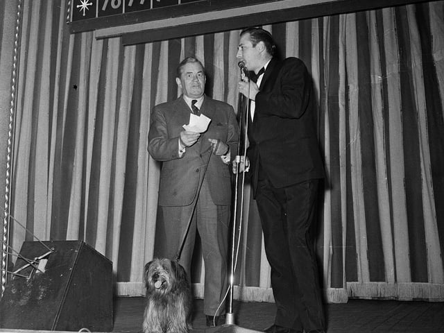 Chief Constable Merrilees is accompanied by the dog that played Bobby in the recently-released Disney film while receiving a charity cheque from the manager of the Mecca Empire Bingo Club in October 1964.