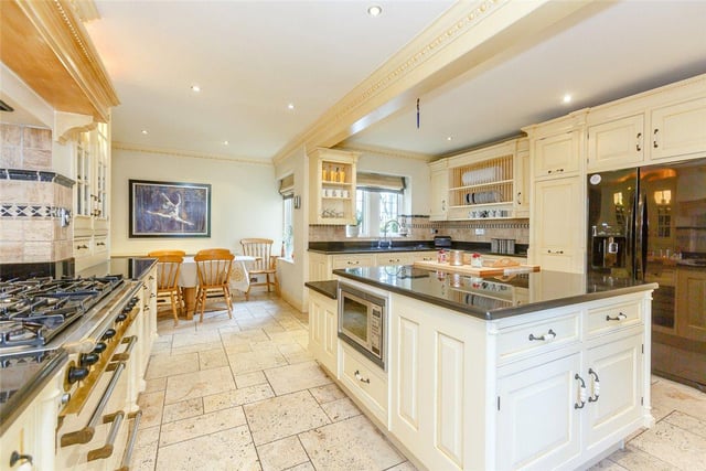 The large country-style kitchen features a range of fitted cream wall and base units, a central island and integrated appliances, including a range cooker, six ring gas hob and fridge freezer.