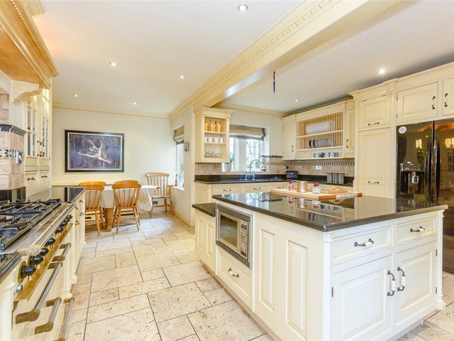 The large country-style kitchen features a range of fitted cream wall and base units, a central island and integrated appliances, including a range cooker, six ring gas hob and fridge freezer.