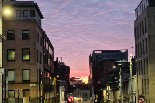 The rising of the pink sun mixed with streetlights glows off the pavements of Glasgow's city centre.