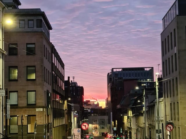 The rising of the pink sun mixed with streetlights glows off the pavements of Glasgow's city centre.