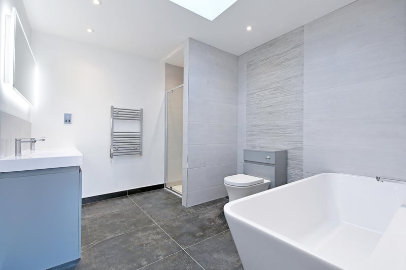 There’s a suite in white, which includes a low-level WC and two wash hand basins. To one corner, there’s a separate shower enclosure with a fitted rain head shower and a glazed screen/door.