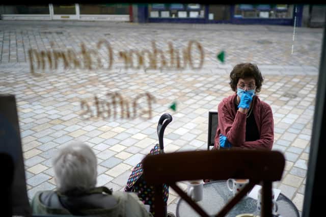 A woman wearing a protective face mask sits outside a cafe (Photo by Christopher Furlong/Getty Images)