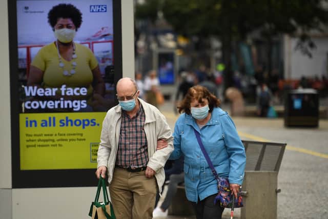 Shoppers wearing face masks walk past a sign calling for the wearing of face coverings in shops, in the city centre of Sheffield. (Photo by OLI SCARFF/AFP via Getty Images)