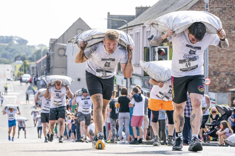 Competitors take part in the Scottish Coal Carrying Championships through the streets of Kelty in Fife.  Picture date: Saturday August 28, 2021. PA Photo. The annual event is one of only two Coal Races in the world and the men's race requires participants to carry a 50-kilo bag of coal and the women's race requires a 25-kilo bag of coal to be carried over 1000 metres through the village. Photo credit should read: Jane Barlow/PA Wire 
