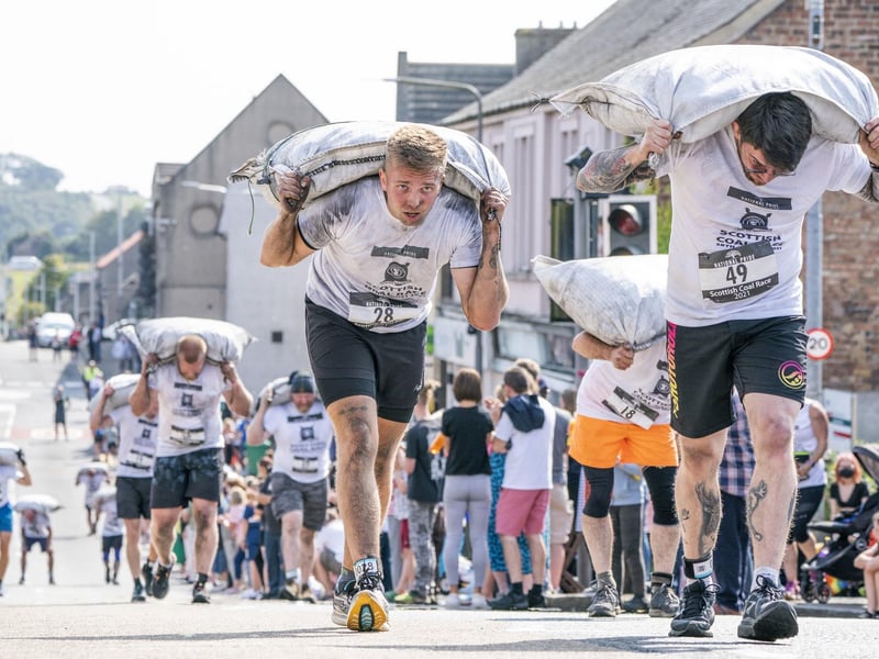 Competitors take part in the Scottish Coal Carrying Championships through the streets of Kelty in Fife.  Picture date: Saturday August 28, 2021. PA Photo. The annual event is one of only two Coal Races in the world and the men's race requires participants to carry a 50-kilo bag of coal and the women's race requires a 25-kilo bag of coal to be carried over 1000 metres through the village. Photo credit should read: Jane Barlow/PA Wire 
