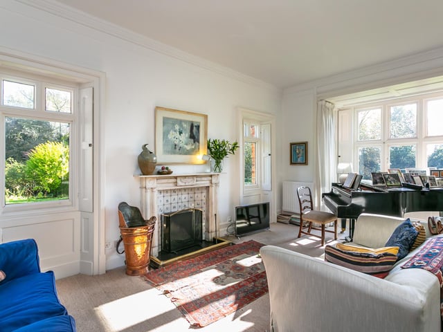 The combined sitting room and lounge provides a snug space in which to relax, with the room bathed in plenty of light from the many windows, and an ornate tiled fireplace serving as the focal point.