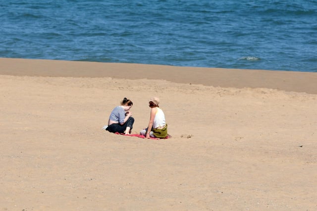 Two people can be seen socially distancing while sitting in the sun.