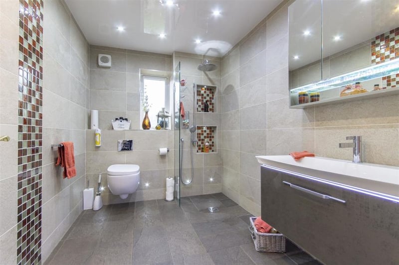 The contemporary wet room is fully tiled with a shower area with digital mixer shower, wall-hung wash hand basin with concealed lighting and storage below, and wall-hung, low-flush WC.