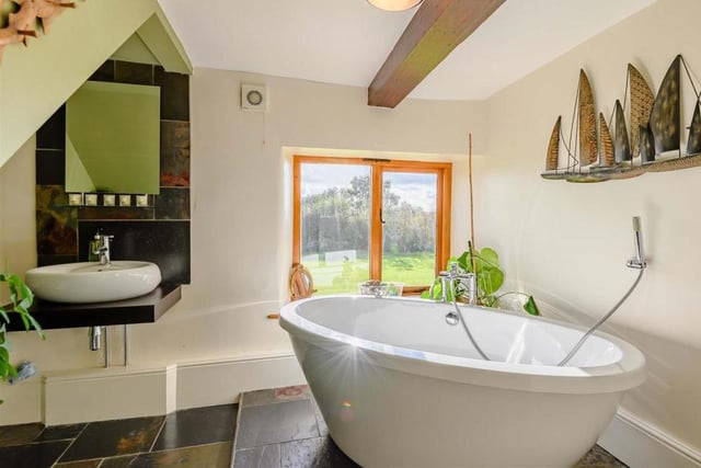 A beautifully-appointed family bathroom that boasts a contemporary four-piece suite, the highlight of which is a large, oval-shaped bath-tub. There is a also a separate, tiled shower-enclosure with a 'rain' shower and an oval-shaped sink mounted on a wall-hung work surface. A slate tiled floor and beamed ceiling add to the room's appeal.