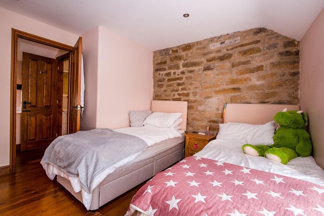 Bedroom two has a stripped wooden floor, double wooden doors opening to a storage area, views over the courtyard and an exposed stone wall.