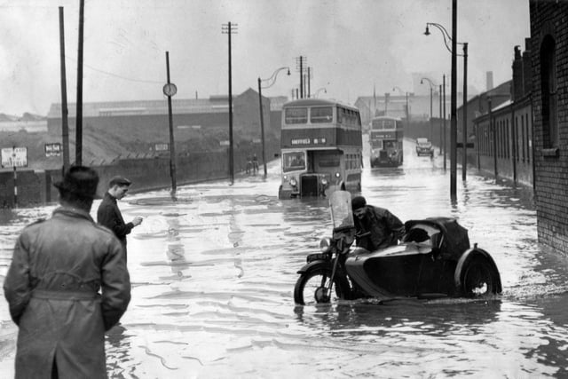 A motor cyclist pushes his combination out of the flood water at the Sheffield and Rotherham boundary - and behind is a Rotherham bus stuck in the water - August 1954
