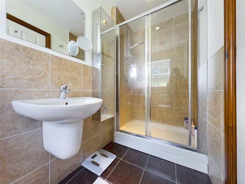 Ensuite shower room with white suite comprising low level WC, wall mounted wash basin and tiled shower enclosure with mixer shower.
