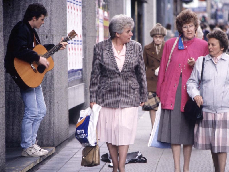 Women walk past a busker in Glasgow, August 1990.