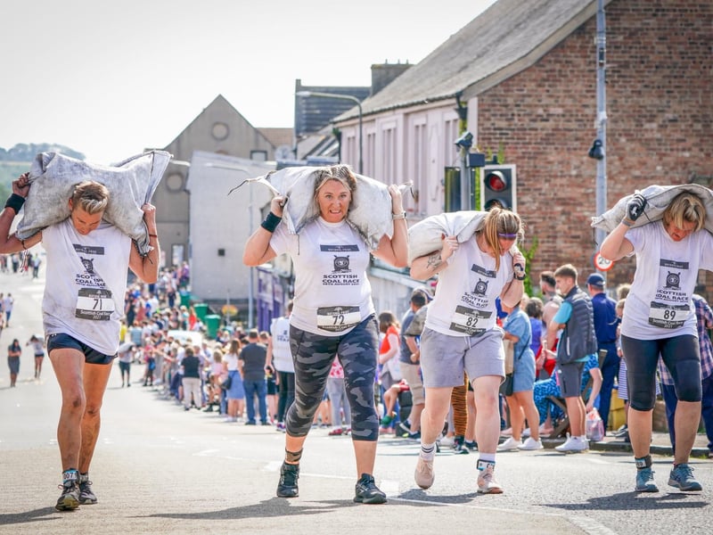 Competitors in the Women's Race take part in the Scottish Coal Carrying Championships through the streets of Kelty in Fife. Picture date: Saturday August 28, 2021. PA Photo. The annual event is one of only two Coal Races in the world and the men's race requires participants to carry a 50-kilo bag of coal and the women's race requires a 25-kilo bag of coal to be carried over 1000 metres through the village. Photo credit should read: Jane Barlow/PA Wire
