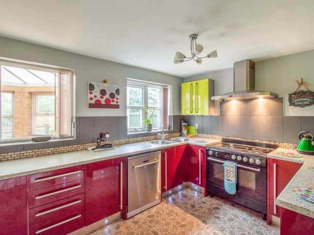 A modern kitchen fitted with a range of high gloss wall and base units with coordinating work surfaces housing the sink and drainer with mixer tap. The kitchen has space for a five ring electric hob with a cooker hood above, an electric oven and grill, plumbing for a dishwasher and space for an American style fridgefreezer. There is plinth under unit lighting and an area for a dining table and chairs. The room has a lot of natural light with two rear facing double glazed windows and a rear facing set of French doors which lead into the conservatory.