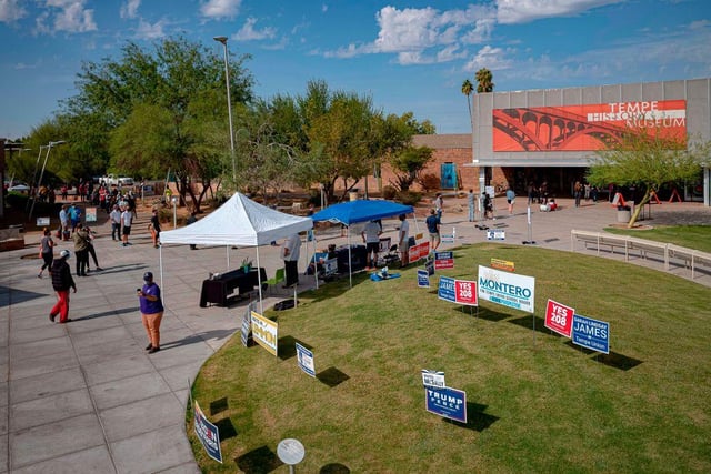 Campaign signs are seen in the grass as people wait in line to vote outside a polling place at Tempe History Museum, in Tempe, Arizona.