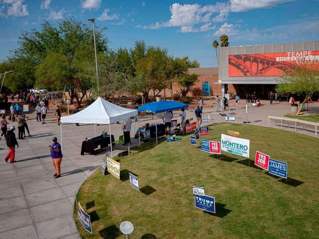 Campaign signs are seen in the grass as people wait in line to vote outside a polling place at Tempe History Museum, in Tempe, Arizona.
