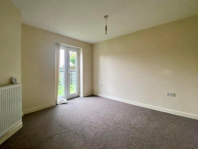 Here is the first bedroom, which has patio doors to the side of the building. The floor is carpeted and the room has plenty of warmth thanks to a double radiator.