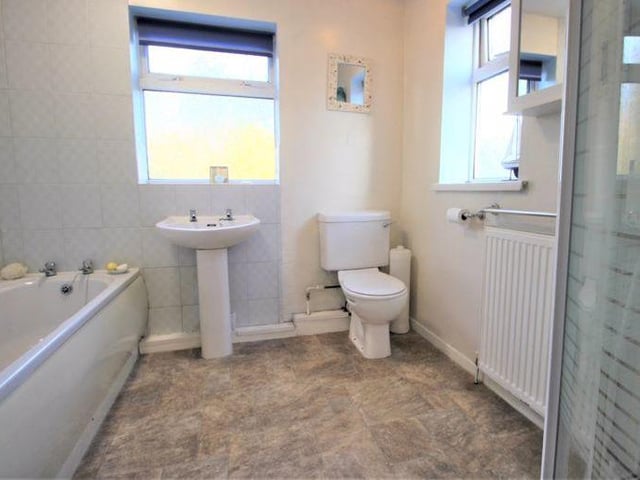 A white, three-piece suite, comprising a hand wash basin, WC and panel bath, makes up the family bathroom at the Ollerton property. This is complemented by a quadrant enclosure that houses an electric shower with glass screen.
