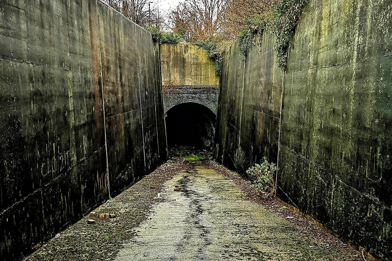 A concrete ramp, hemmed in on both sides by concrete walls, leads to the tunnel entrance.