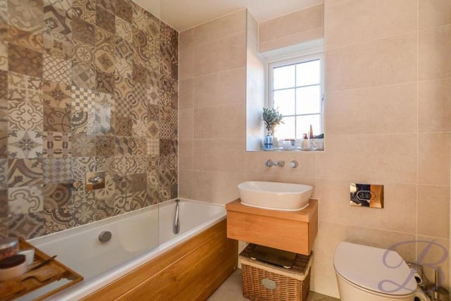 The first floor also houses this bathroom, which includes a panelled bath and chrome shower. Other assets are a wash hand basin with vanity unit, a low-flush WC, opaque window and full-height tiling with a feature wall.