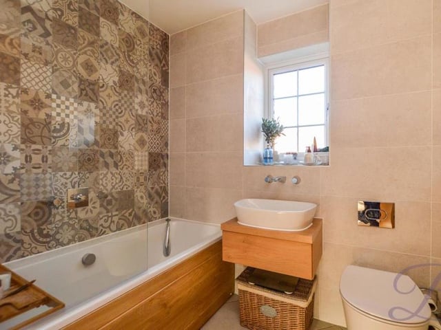The first floor also houses this bathroom, which includes a panelled bath and chrome shower. Other assets are a wash hand basin with vanity unit, a low-flush WC, opaque window and full-height tiling with a feature wall.