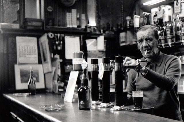 Willie Ross, proprietor of the Oxford Bar, pours a drink behind the bar in 1982.