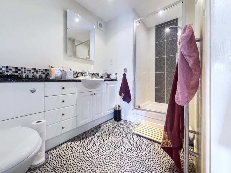 En Suite - Modern white suite comprising low level WC with concealed cistern, inset wash basin, vanity cupboards, splash-back tiling, tiled shower enclosure with electric shower unit; inset spot lighting, Karndean flooring, extractor fan and towel radiator.