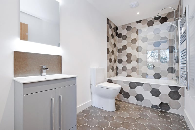There’s a suite in white, which includes a low-level WC and a wash hand basin, storage beneath and illuminated vanity mirror above. To one corner, there’s a fully tiled bath with a chrome mixer tap, fitted rain head shower, an additional hand shower facility and a glazed screen.