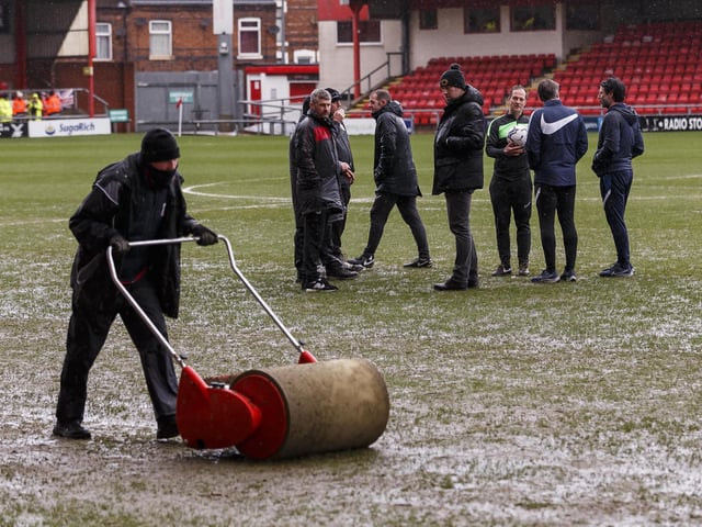 A groundsman at Gresty Road gets to work on the pitch as referee Martin Coy chats to Danny and Nicky Cowley and Crewe boss David Artell