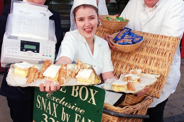 Orders for cakes and sandwiches  were being taken by fax and e-Mail at the Cake Box back in 2000. In the bike hamper is Leanne Carter-Ashton, holding the fax machine is Carol Parratt, on the bike is Douglas Parratt and holding the snacks is Dawn Flegg.