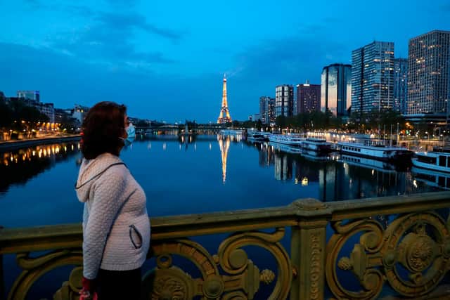 A woman wearing a protective mask looks at the Eiffel tower and its reflection on the Seine river in Paris (Photo by LUDOVIC MARIN/AFP via Getty Images)