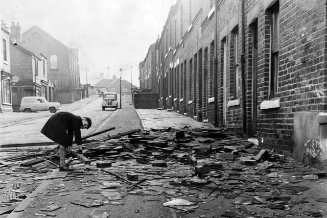 An inquisitive schoolboy bends to get a closer look at the wreckage of roof slates and wood strewn over the pavement of School Street, Rotherham. The area was hit by hurricane-strength winds on February 16, 1962