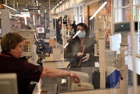 A woman wearing PPE stands behind a perspex screen as she is served by a worker at a supermarket till (Photo by Oli SCARFF / AFP) (Photo by OLI SCARFF/AFP via Getty Images)